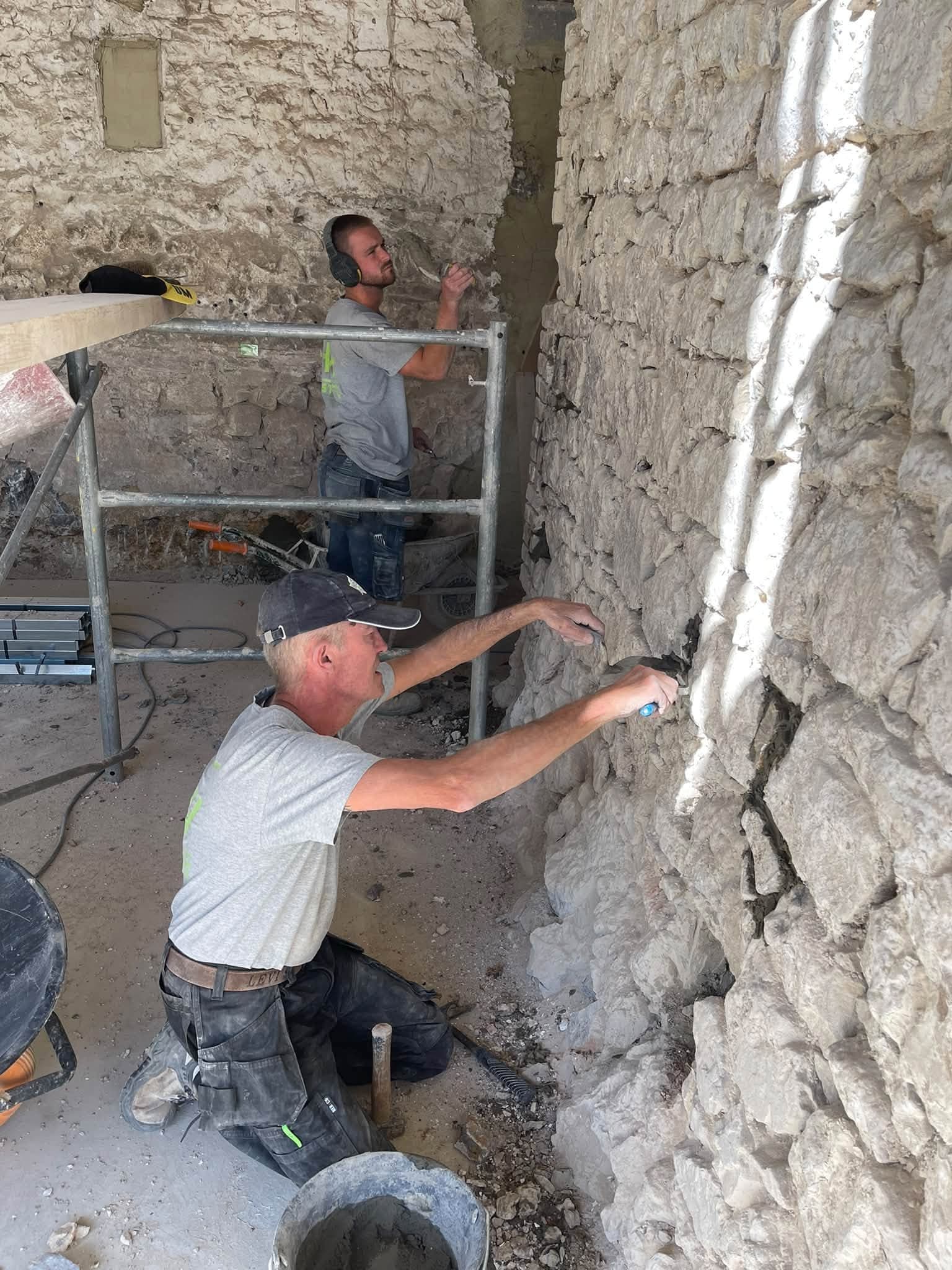 Artisan rejointoyant un mur en pierre depuis un échafaudage