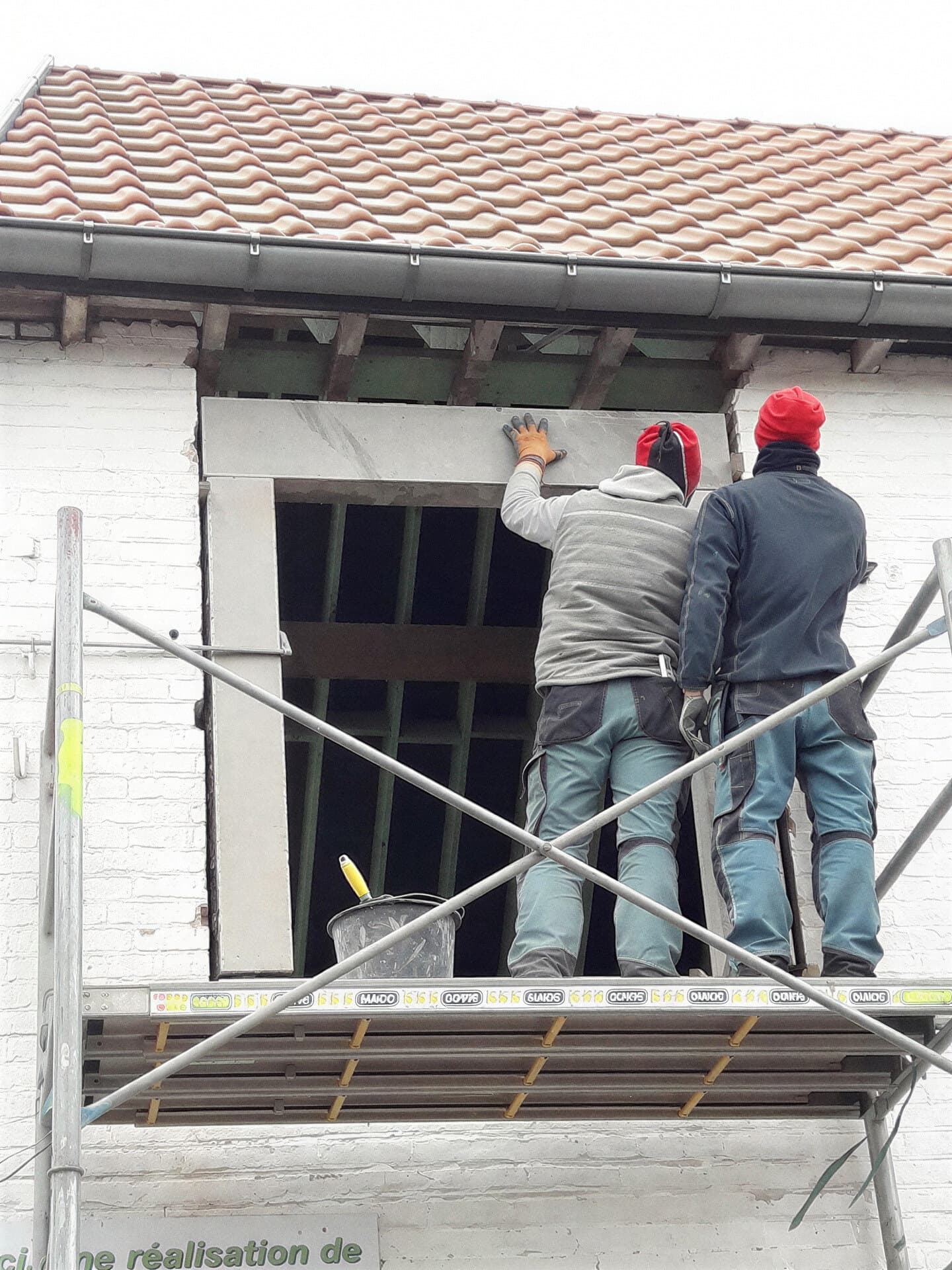 Deux artisans sur un échafaudage devant une façade enduite de blanc