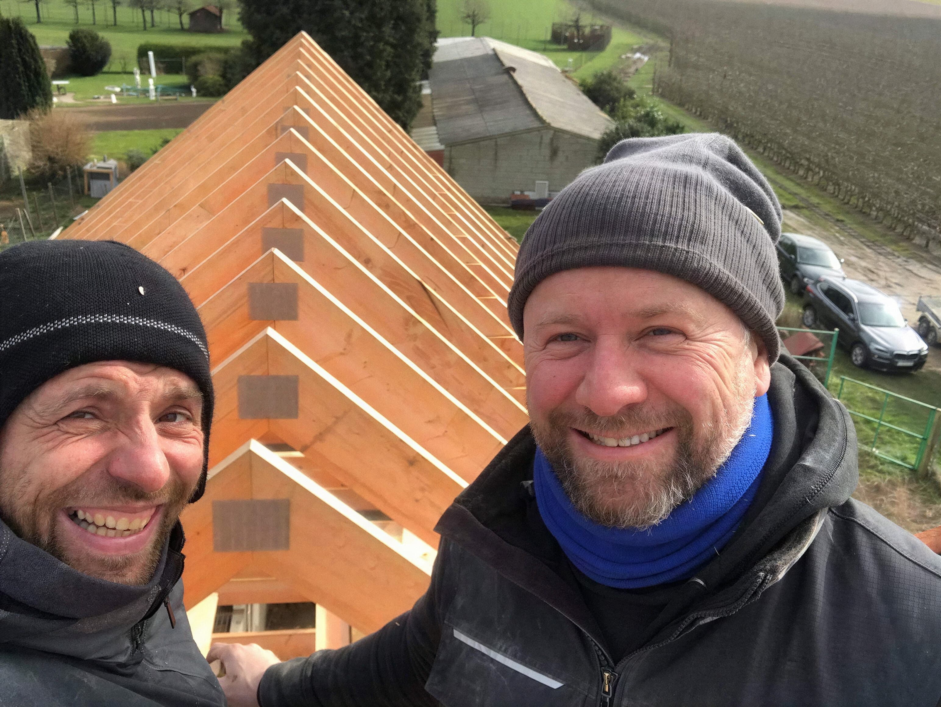 Deux artisans de l’équipe souriants devant une charpente en bois