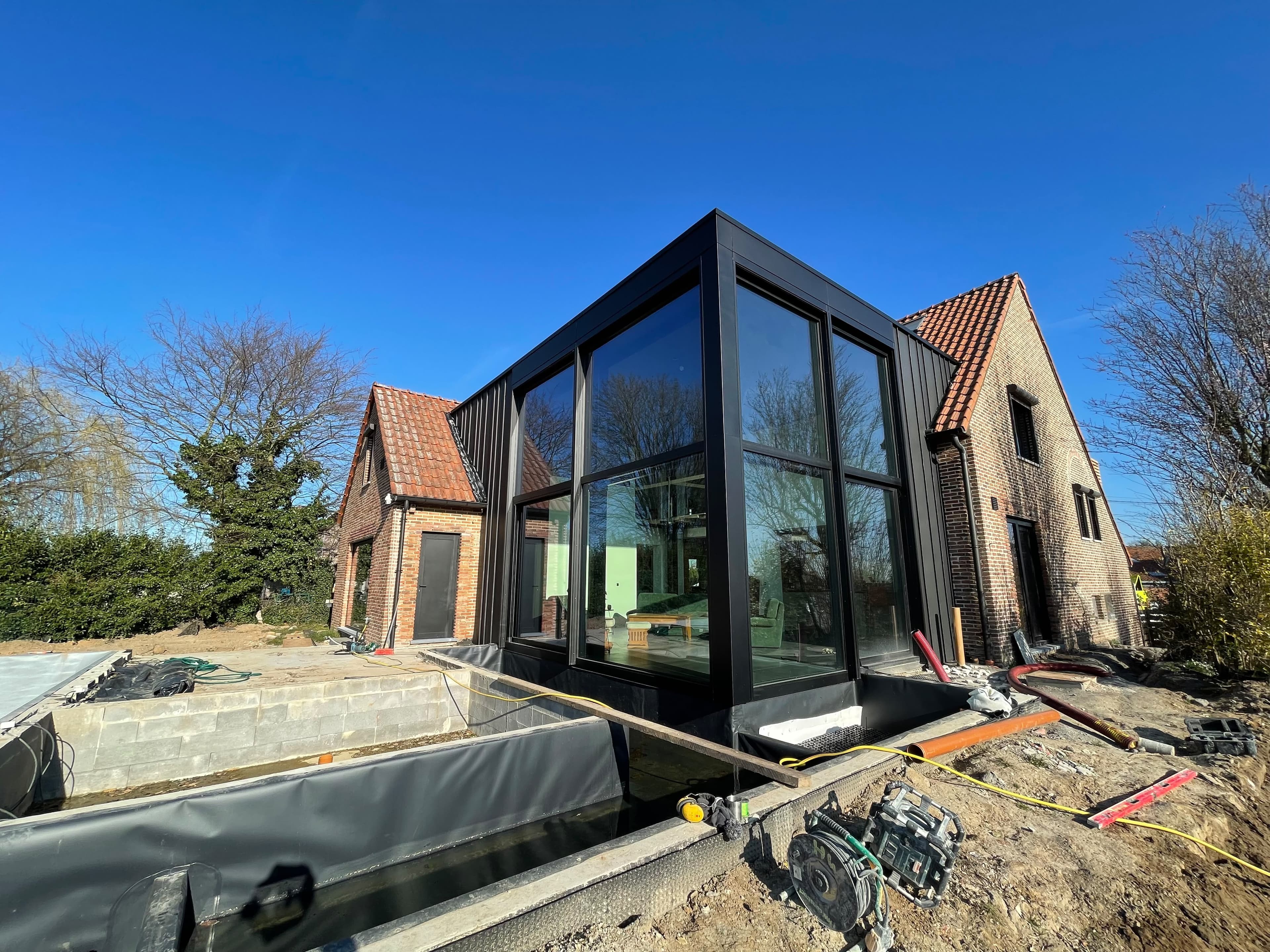 Extension vitrée à structure noire accolée à une maison en briques