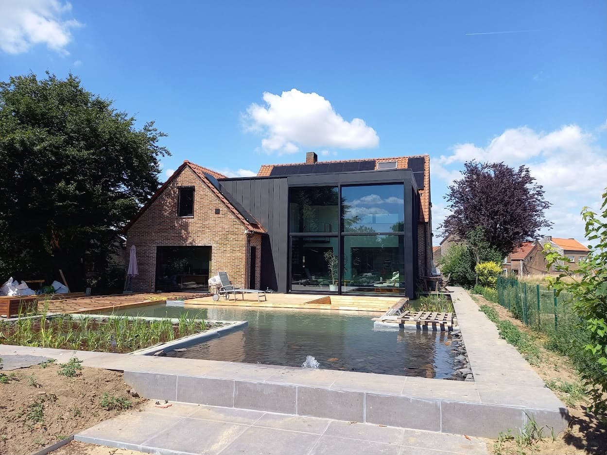 Extension vitrée contemporaine et bassin devant une maison en briques