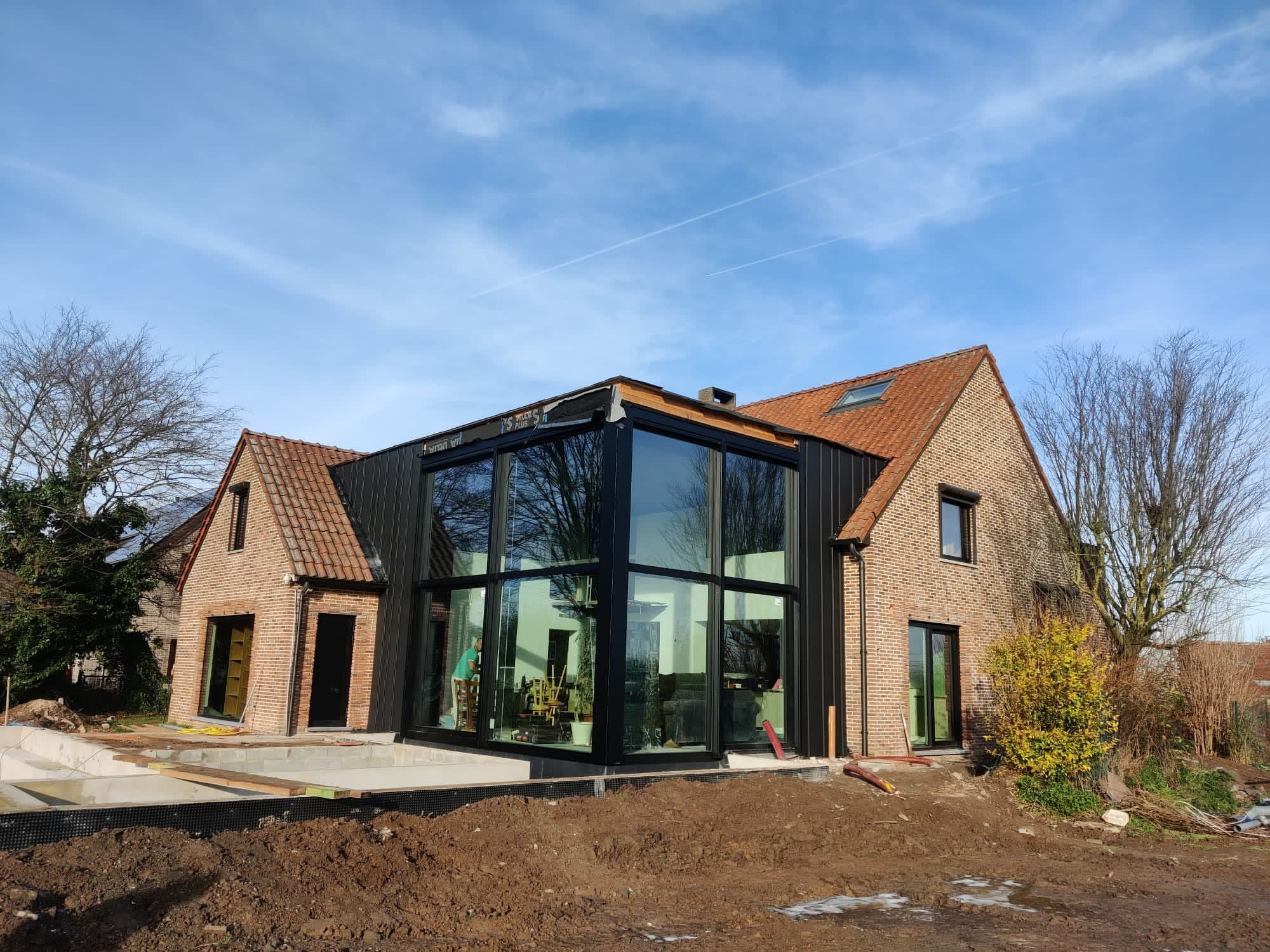 Extension vitrée à structure noire accolée à une maison en briques
