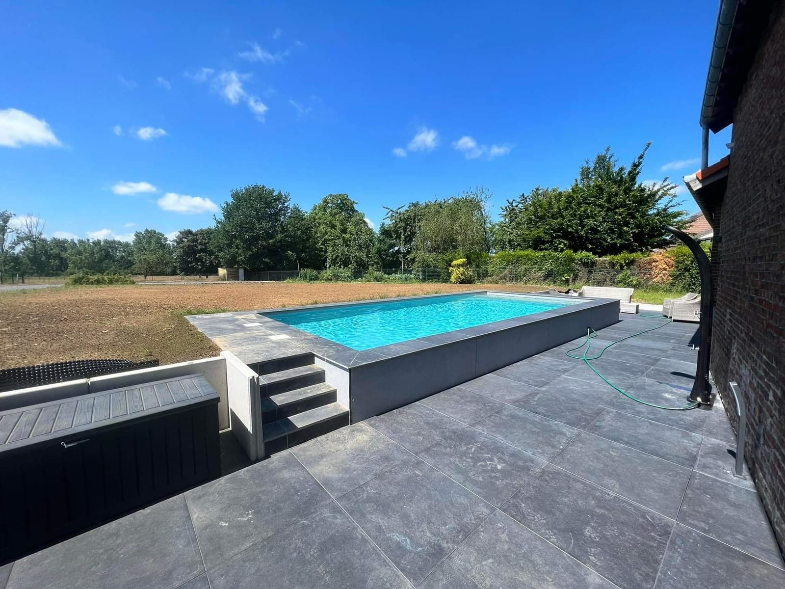Piscine maçonnée et grande terrasse en pierre bleue au pied d’une ferme en briques