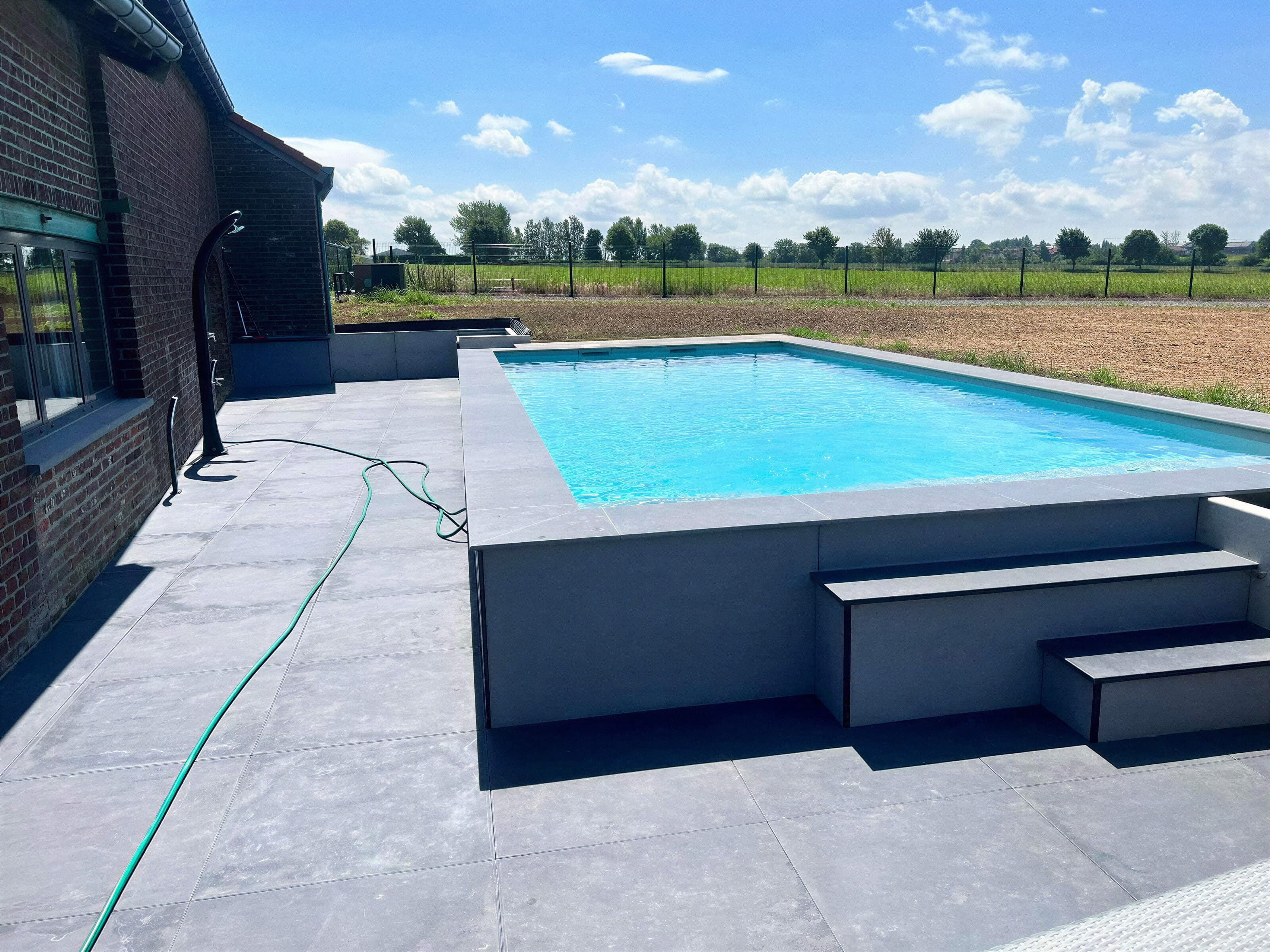 Grande terrasse en dalles et piscine maçonnée au bord des champs